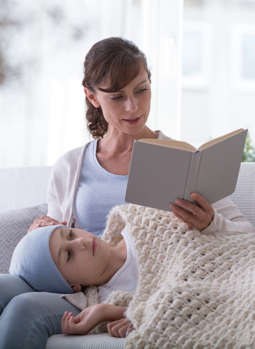 Mother reading book to weak child with leukemia during treatment